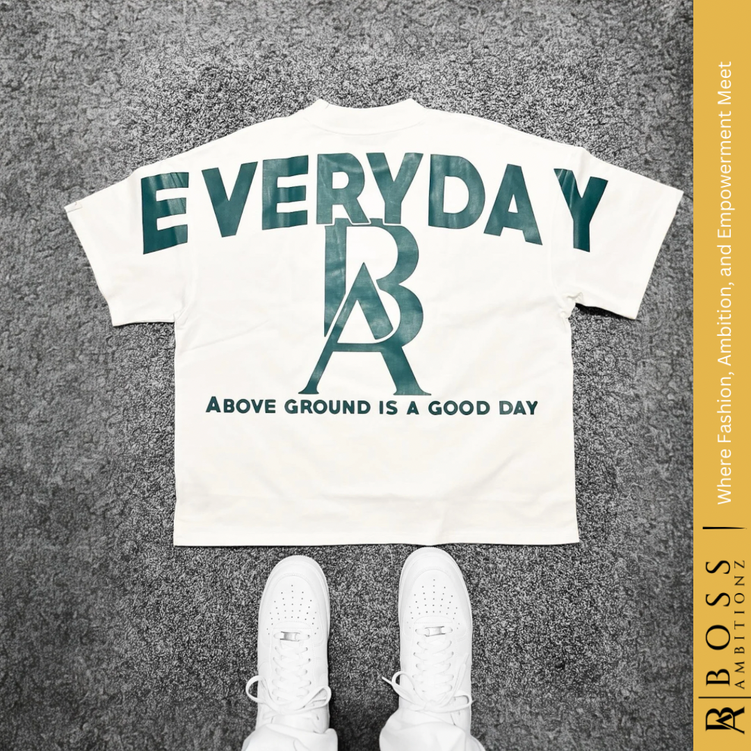 Oversized heavyweight cotton tee in white, featuring 'Boss Ambitionz' in a circular formation around a graphic of praying hands on the front, and 'EVERYDAY Above Ground Is A Good Day' in bold green text on the back