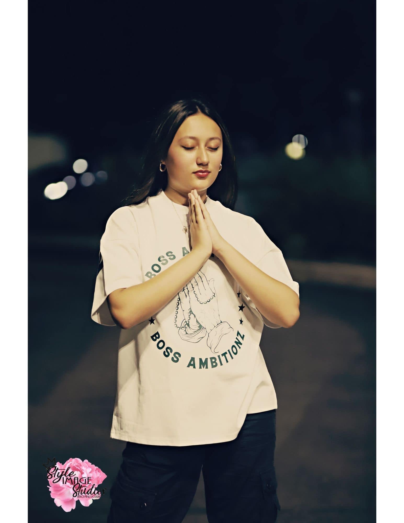 Miss Junior Teen United USA stands serene in the night, her hands clasped in prayer, wearing the Boss Ambitionz Everyday Luxe Oversized T-Shirt. The image captures a moment of reflection, highlighted by the iconic praying hands logo of Boss Ambitionz. Visit our website to explore the full collection at www.bossambitionz.com.