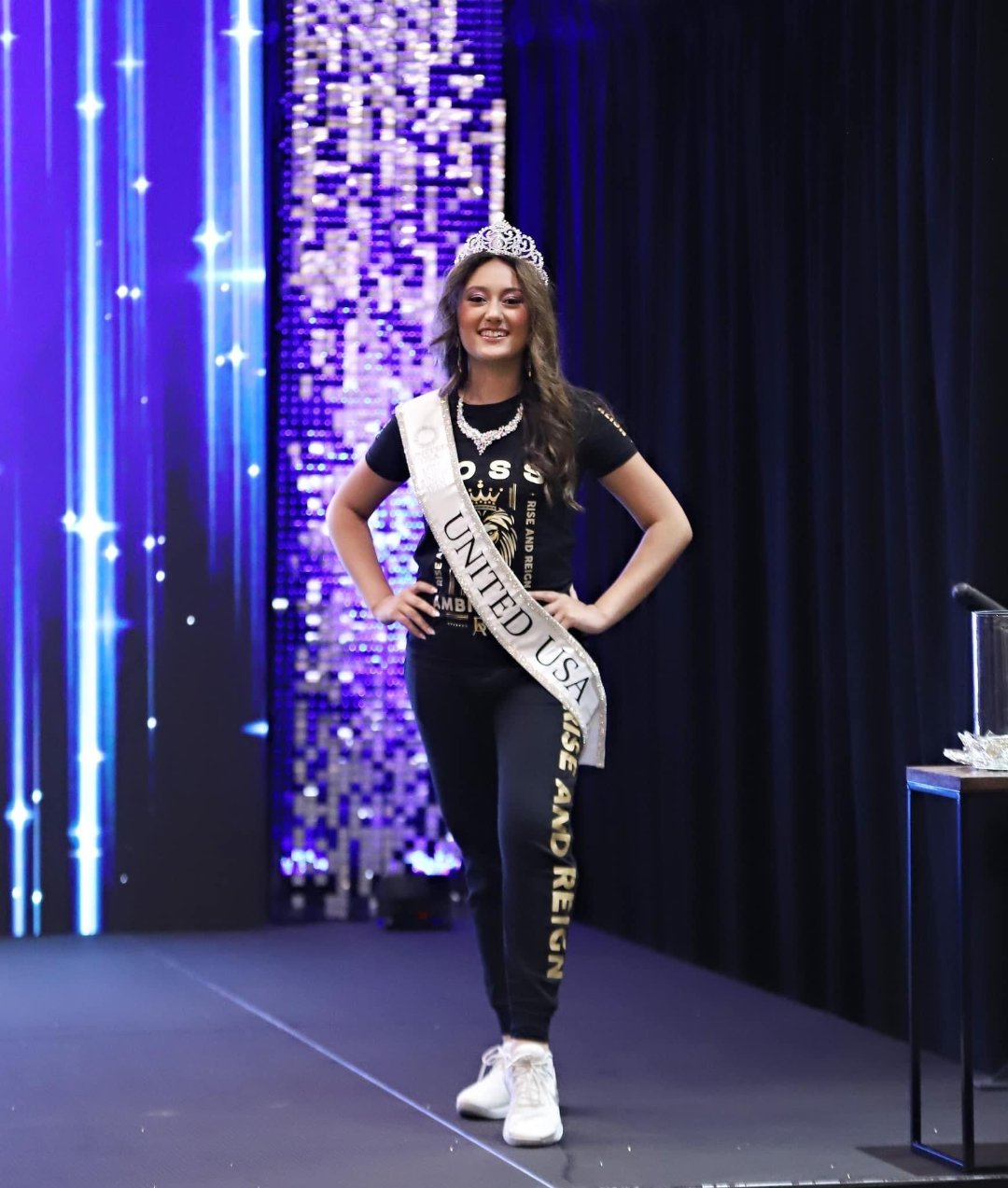 Rihana walking gracefully on stage at the United USA National Pageant in Daytona Beach, FL, in her Regal Lioness Tee from Boss Ambitionz. She exudes confidence and style, with the vibrant backdrop adding to the event's grandeur