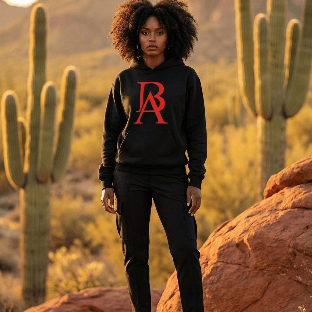 Black female model wearing a black boss leader dreamer hoodie with a red logo in a desert setting with cacti and rocks.