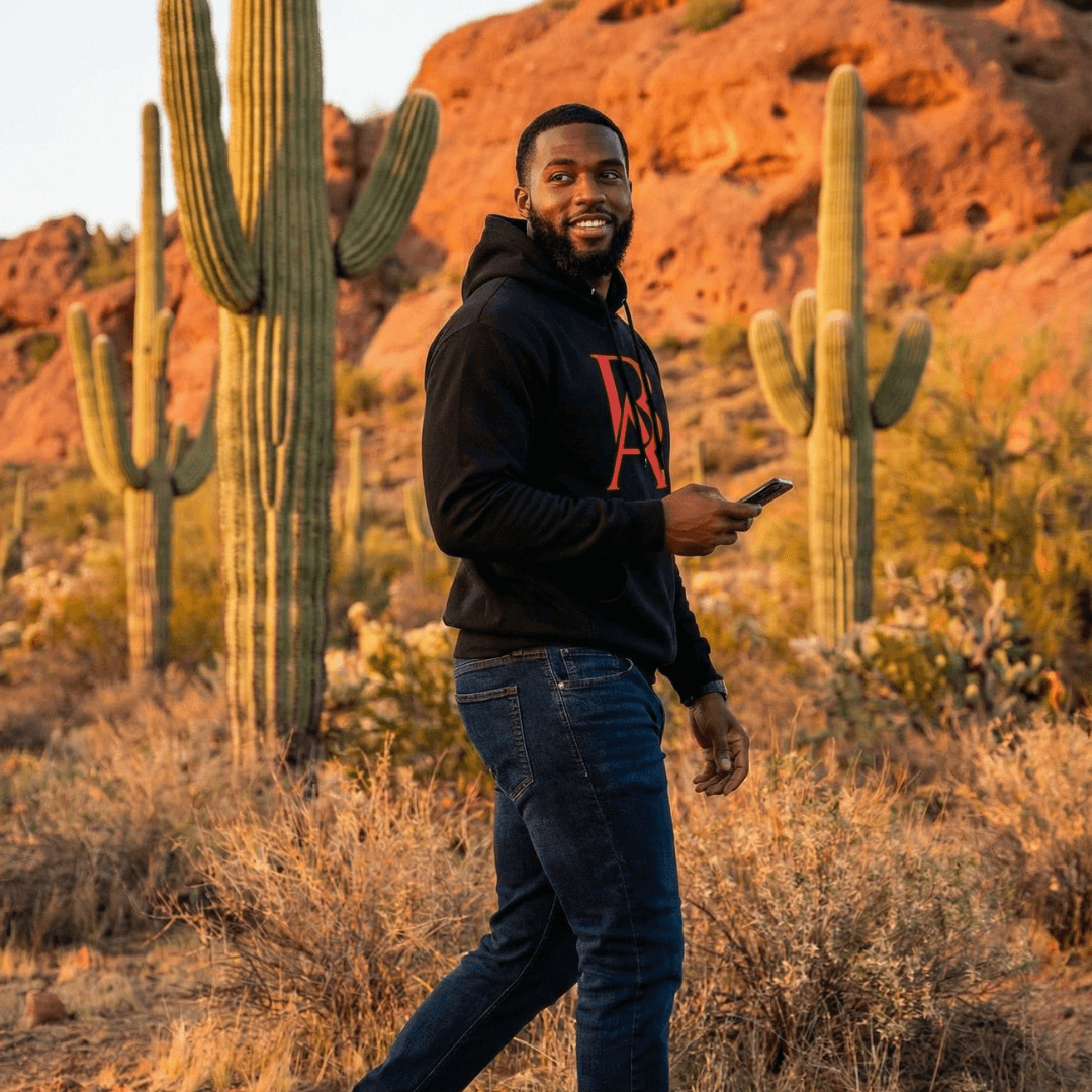 Man in a black boss leader dreamer hoodie with red logo standing in a desert landscape with cacti.