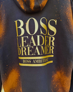 Back view of the Rustic Hustlers Rhinestone Hoodie showing bold gold lettering that reads “BOSS LEADER DREAMER” and “BOSS AMBITIONZ,”