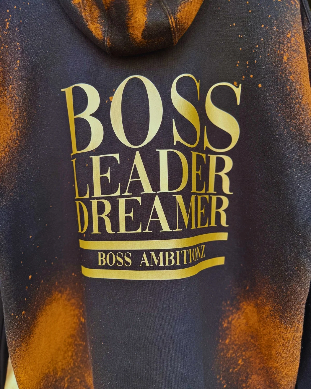 Back view of the Rustic Hustlers Rhinestone Hoodie showing bold gold lettering that reads “BOSS LEADER DREAMER” and “BOSS AMBITIONZ,”