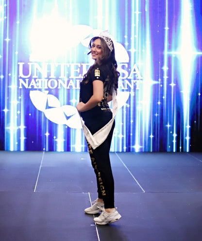 Rihana turning slightly on stage at the United USA National Pageant in Daytona Beach, FL, to showcase the side view of her outfit. She is wearing the Regal Lioness Tee from Boss Ambitionz, complemented by her sash and crown, embodying grace and ambition.