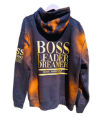 Back view of the Rustic Hustlers Rhinestone Hoodie showing bold gold lettering that reads “BOSS LEADER DREAMER” and “BOSS AMBITIONZ,” on a black hoodie with orange acid-wash pattern and distressed finish.