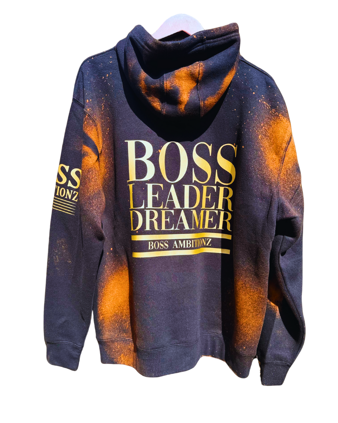 Back view of the Rustic Hustlers Rhinestone Hoodie showing bold gold lettering that reads “BOSS LEADER DREAMER” and “BOSS AMBITIONZ,” on a black hoodie with orange acid-wash pattern and distressed finish.