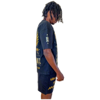 Side profile of model in Boss Ambitionz outfit: "Side profile of model wearing Boss Ambitionz t-shirt and shorts, emphasizing the intricate gold designs and motivational text 'Unleash Your Ambition' on the shorts.