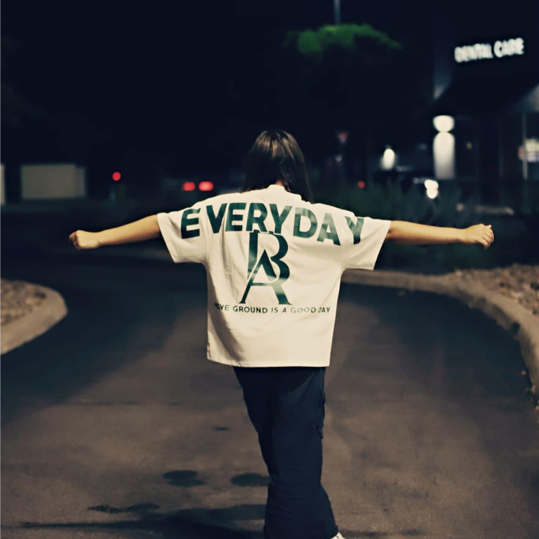 A serene night-time photo capturing Miss Junior Teen United USA standing with her arms outstretched in a Boss Ambitionz 'Everyday Luxe' Oversized T-Shirt. The back of the shirt features the inspiring message "EVERYDAY IS A GOOD DAY" in bold green letters. This image embodies freedom and the celebration of everyday moments. Discover more inspiring fashion at Boss Ambitionz Website.