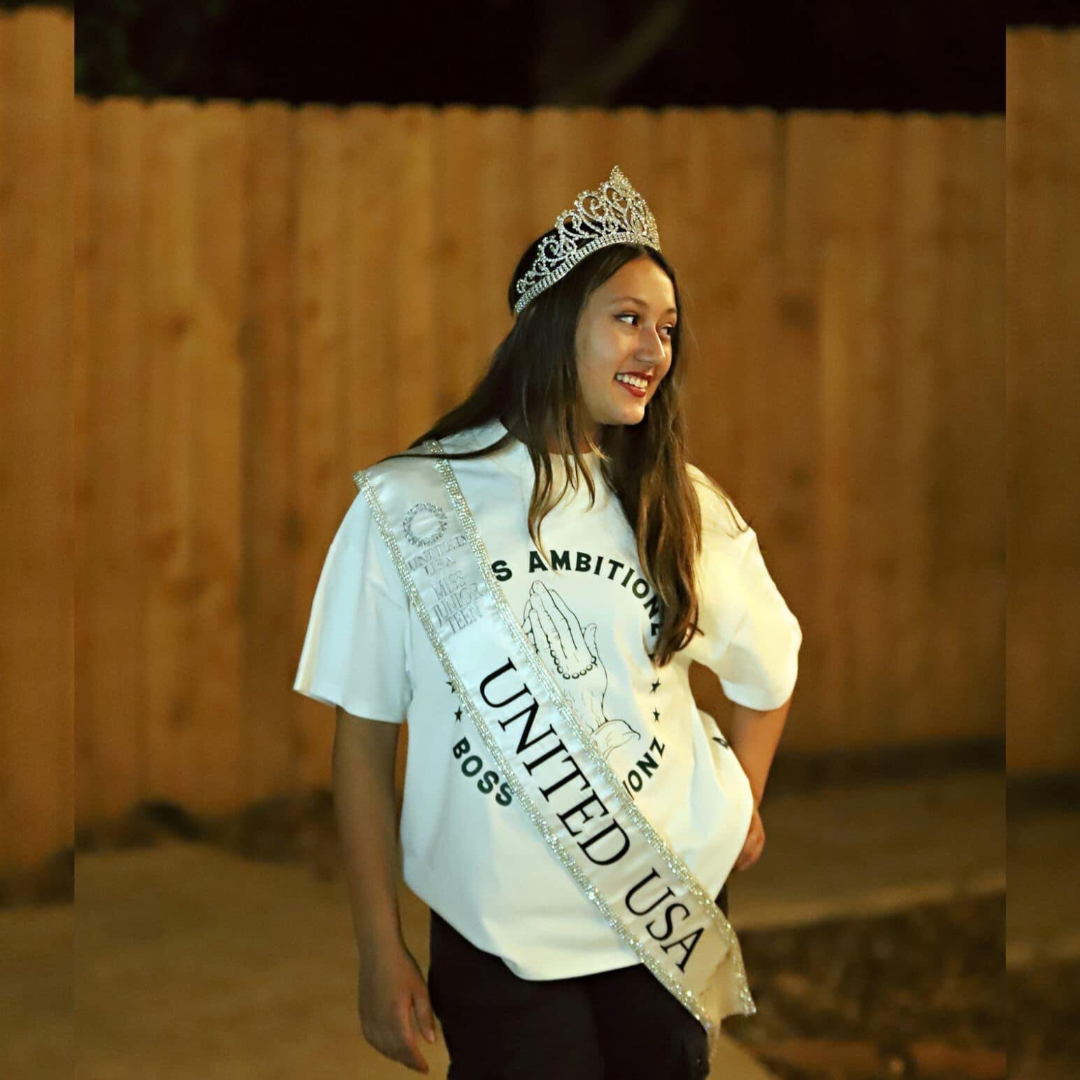Rihana, the current Miss Junior Teen United USA, gracefully poses while wearing the Boss Ambitionz 'Everyday Luxe' oversized T-shirt. She exudes confidence and elegance, showcasing the bold design of the tee paired with her crown and sash. Photo credit: @StyleImageStudios. For more styles, visit Boss Ambitionz