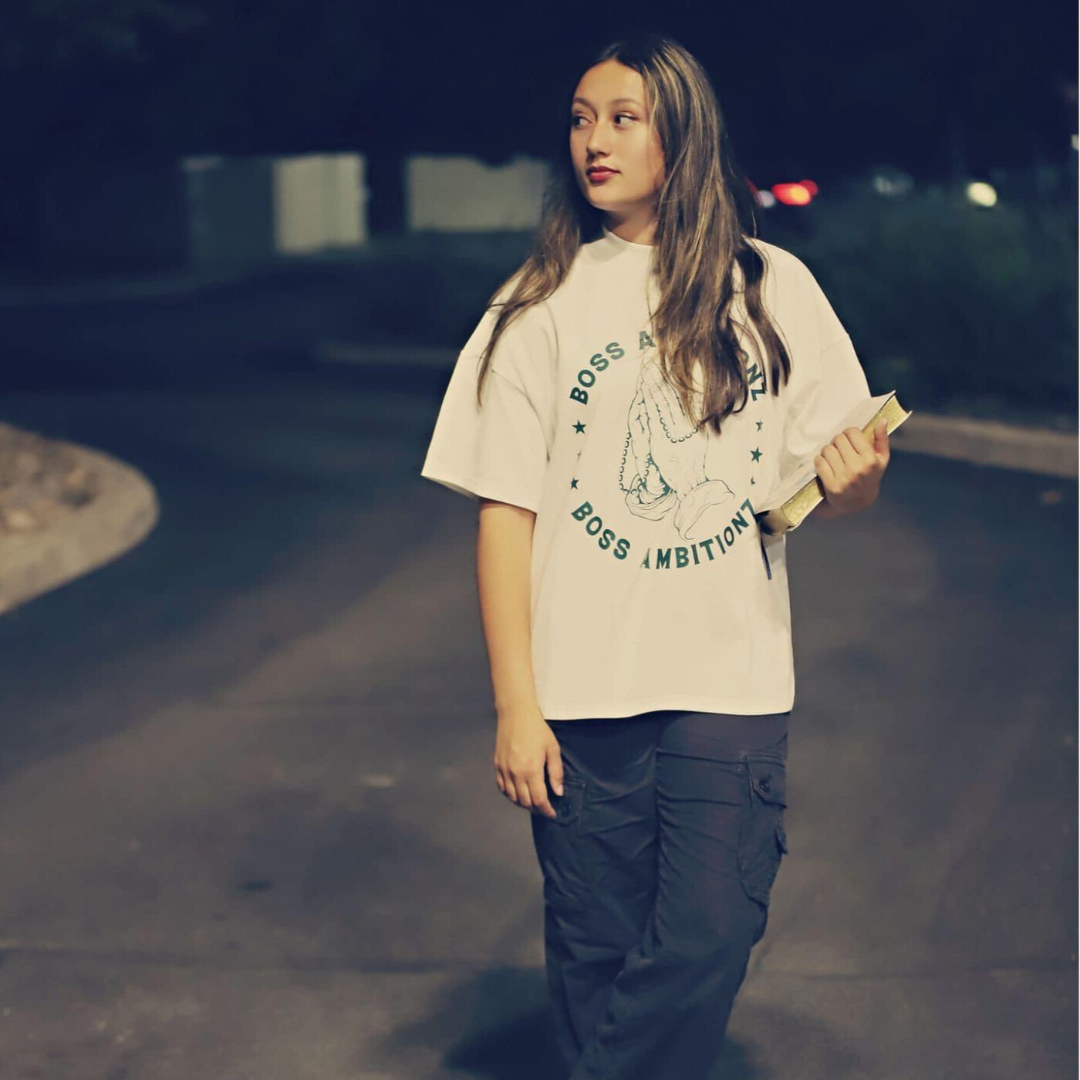 Miss Junior Teen United USA stands confidently in the Boss Ambitionz Everyday Luxe Oversized T-Shirt, holding a book as she gazes into the distance. The backdrop of a quiet night enhances the timeless appeal of this stylish, heavyweight cotton tee. Explore more at www.bossambitionz.com