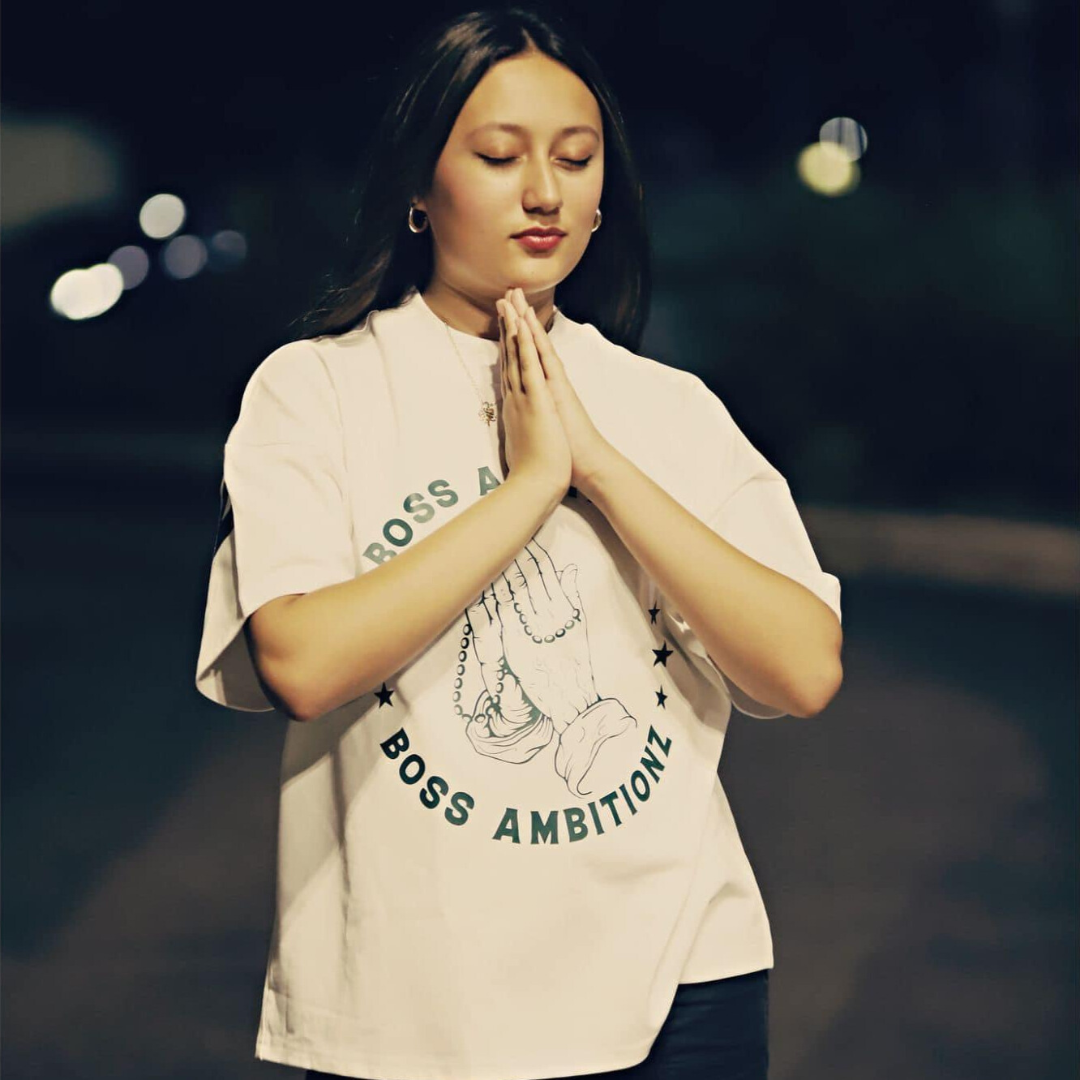 Miss Junior Teen United USA, celebrated pageant winner, showcases the Boss Ambitionz 'Everyday Luxe' Oversized T-Shirt. Her casual style is accentuated by the shirt's bold graphic, featuring an iconic prayer hands design, surrounded by the stars and script that read "BOSS AMBITIONZ". Perfect for those who blend laid-back fashion with a touch of luxury. Visit us at Boss Ambitionz Website to explore more.