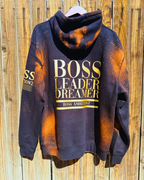 Back view of the Rustic Hustlers Rhinestone Hoodie showing bold gold lettering that reads “BOSS LEADER DREAMER” and “BOSS AMBITIONZ,” on a black hoodie with orange acid-wash pattern and distressed finish.