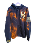 Front view of the Rustic Hustlers Rhinestone Zip-Up Hoodie by Boss Ambitionz, featuring an orange acid-wash finish on black fleece with gold BA logo, rhinestone detailing on the chest, and sleeve branding that reads “BOSS AMBITIONZ.