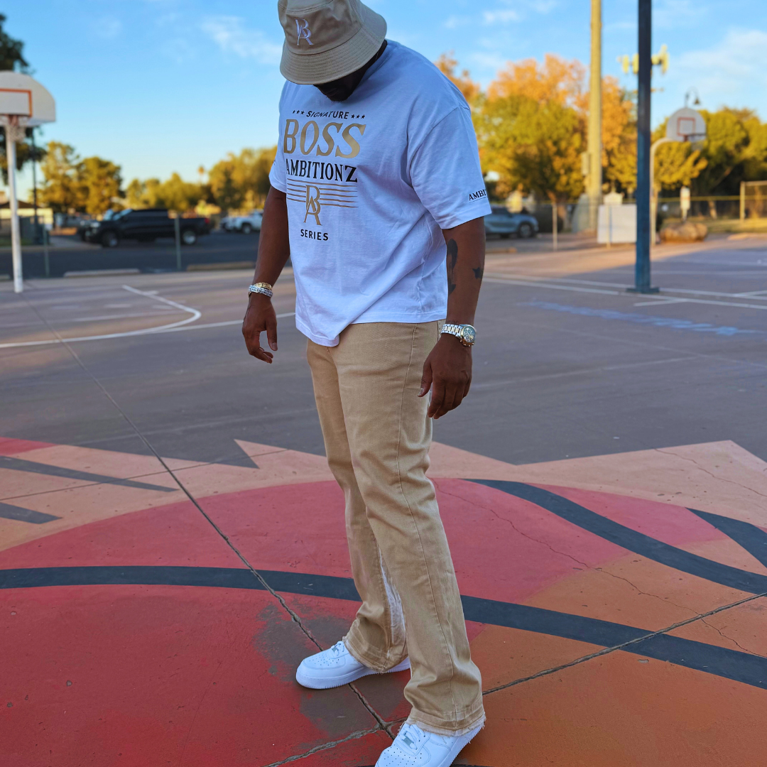 A person wearing a Boss Ambitionz tee and beige pants, standing on a basketball court with a confident posture.